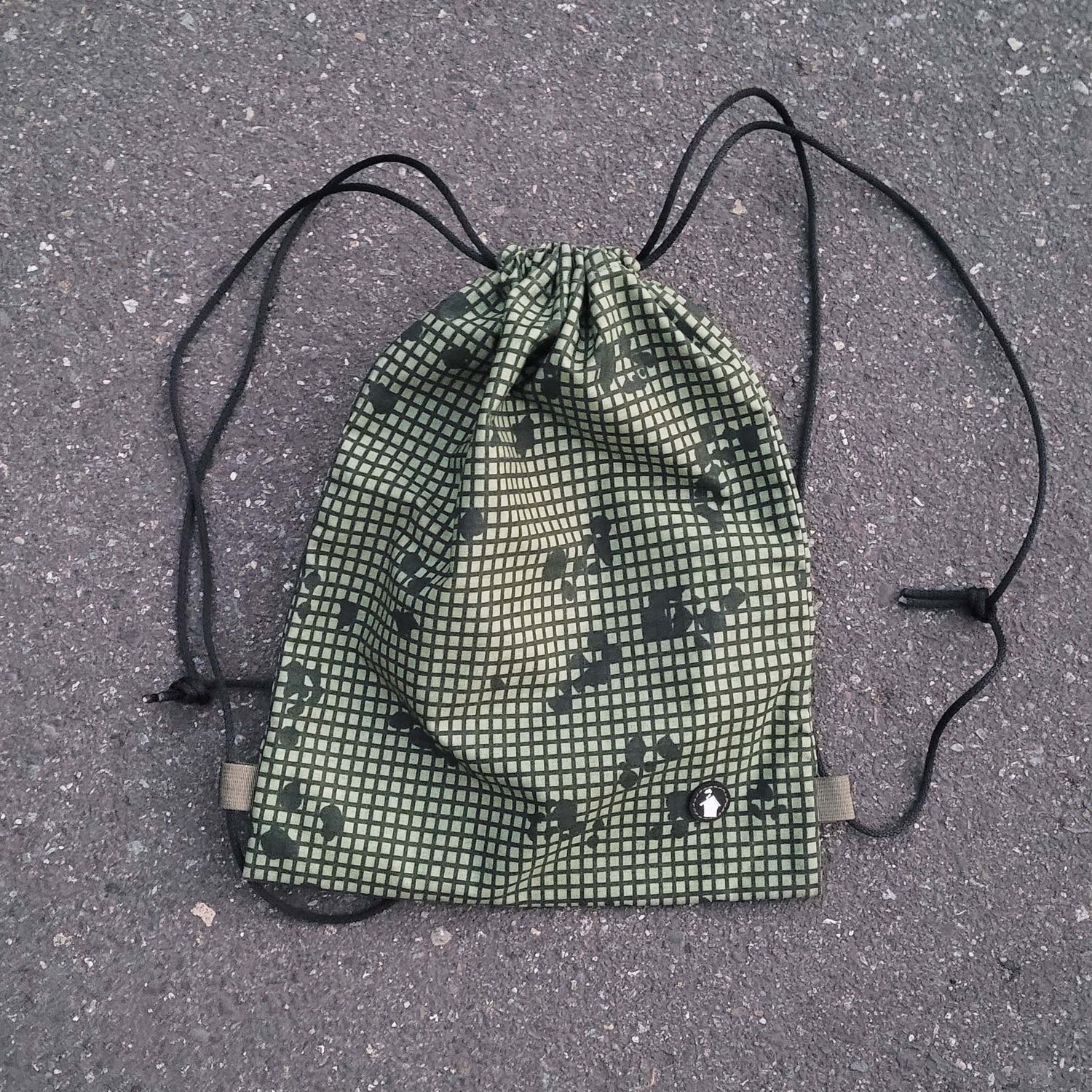 Green drawstring bag with black pattern on a gray pavement