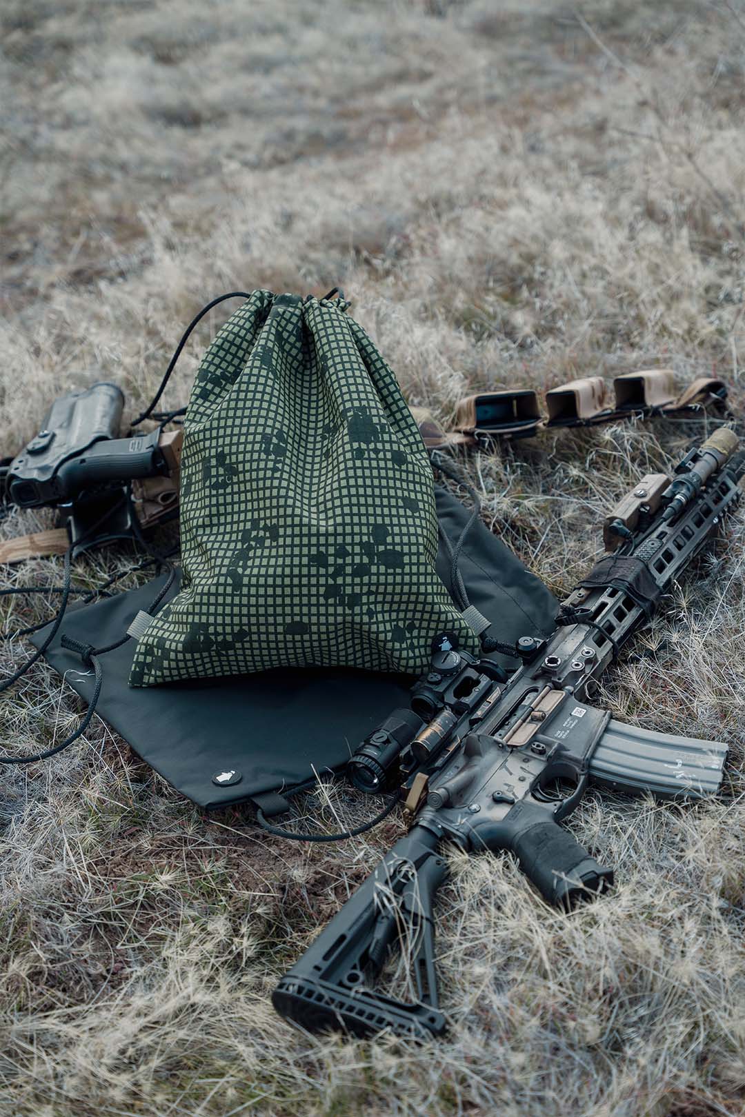 Green camouflage bag and rifle on a grassy field
