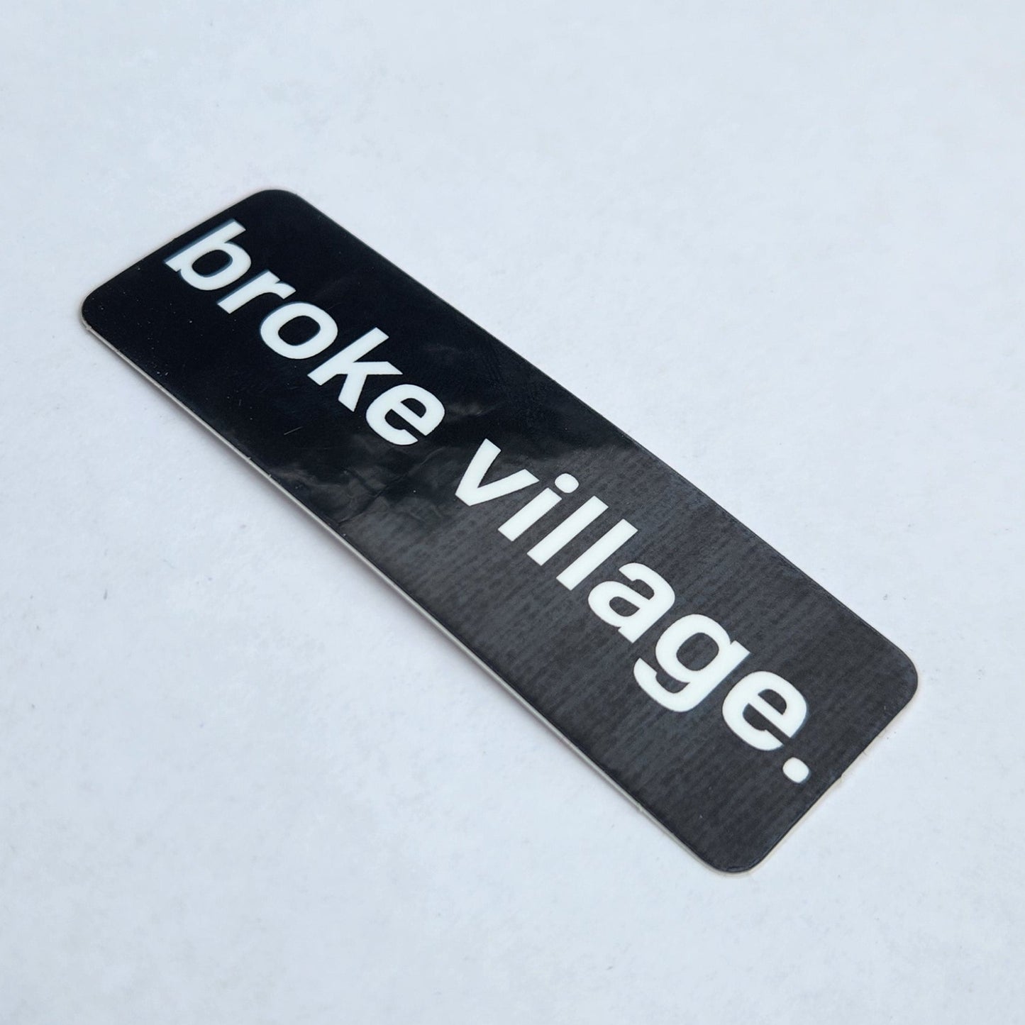 Black and white 'broke village.' sticker on a light gray background