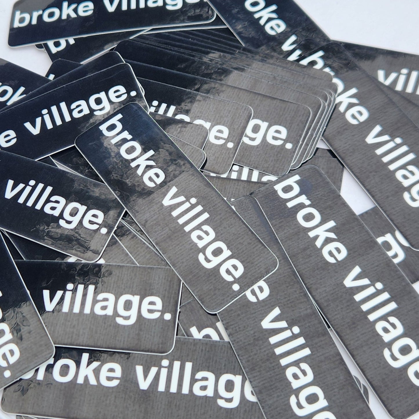 Multiple 'broke village' stickers on a white surface with a blurred background