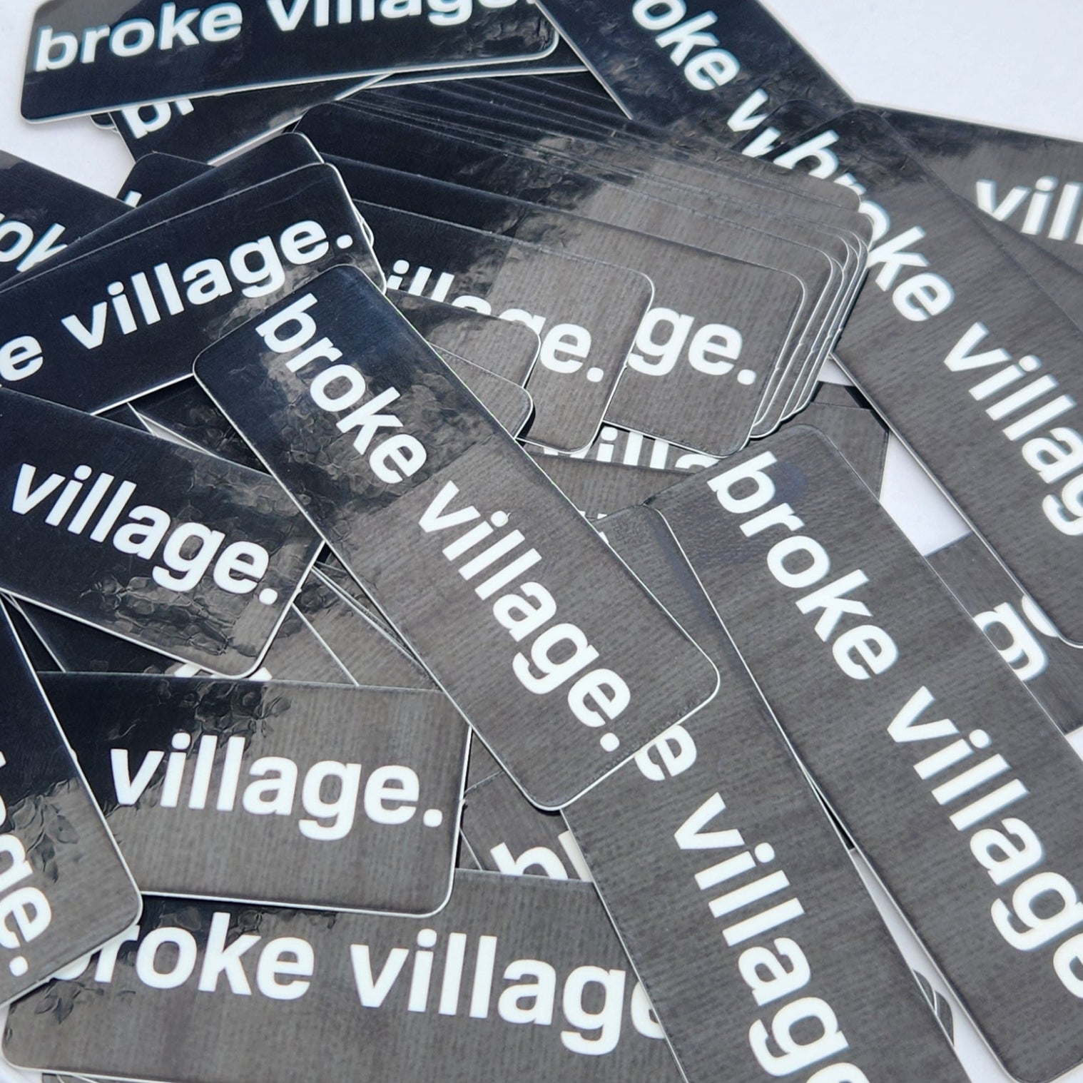 Multiple 'broke village' stickers on a white surface with a blurred background