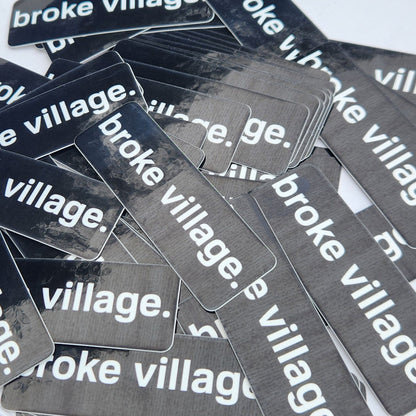 Multiple 'broke village' stickers on a white surface with a blurred background