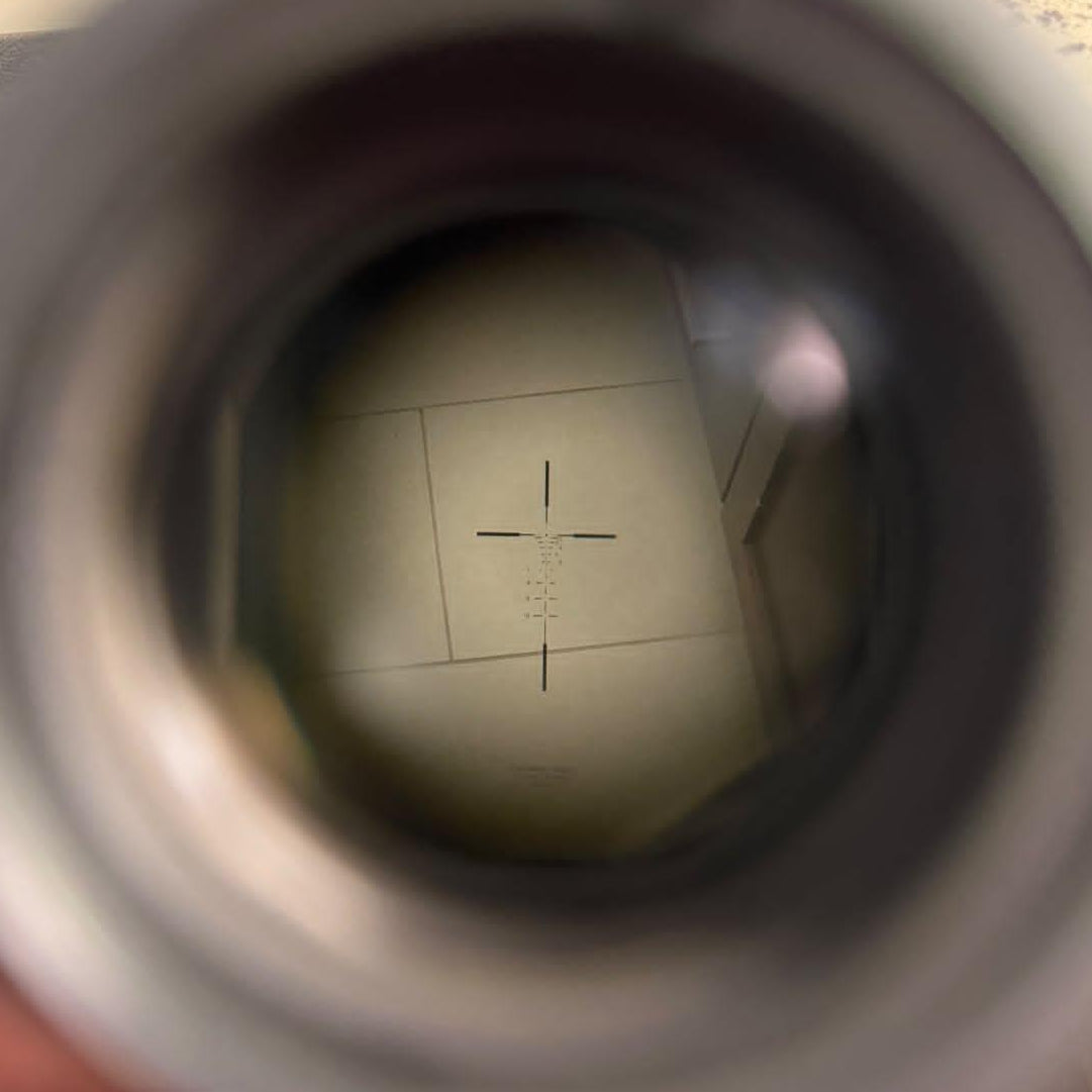 A close-up view through a circular opening of a gray container, showing a bathroom floor and a hand holding the item in a real indoor environment.