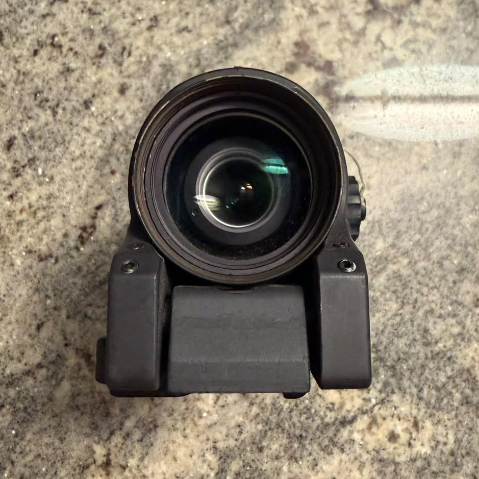 A black tactical sight or camera lens attachment photographed from above on a speckled stone surface.